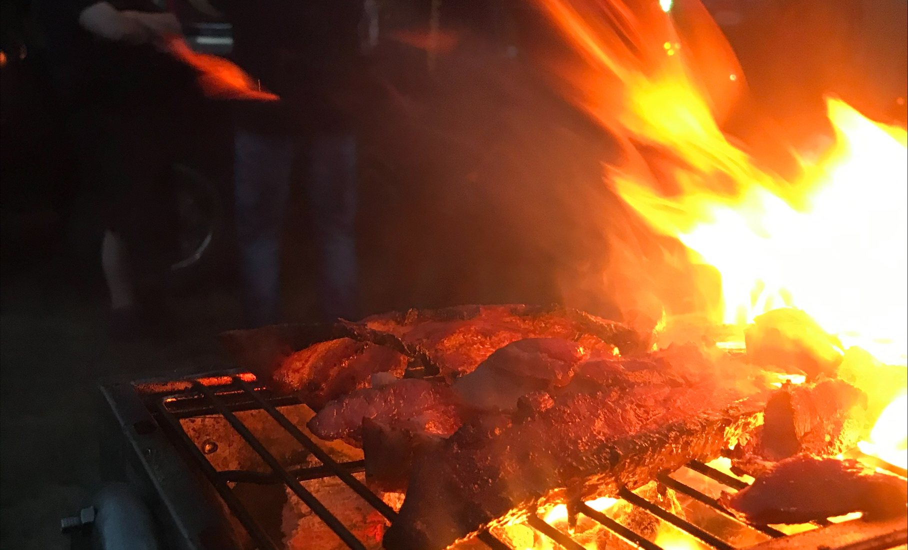 Kött på en flammande grill en kväll, med gäster i bakgrunden