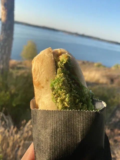 En macka i svart papper hålls upp framför havet i kvällssol